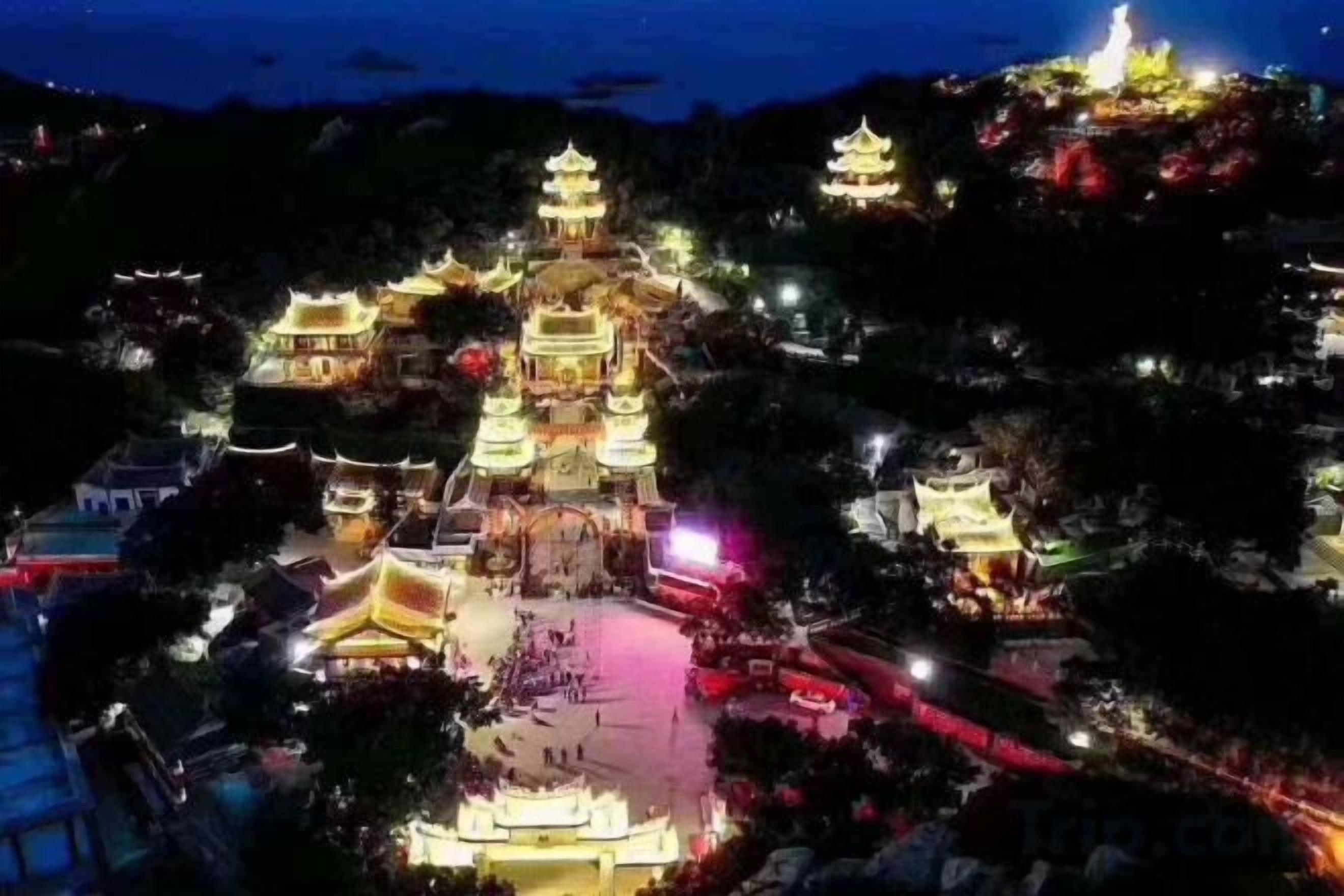 Un edificio tradicional de estilo pagoda, con varios niveles y un patio central, rodeado de árboles e iluminado con luces artificiales.
