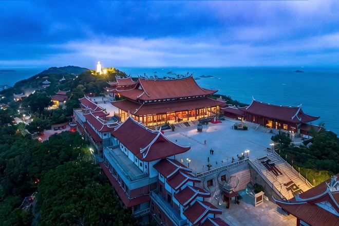 A traditional building with multiple levels and a central courtyard, surrounded by greenery and overlooking a body of water.