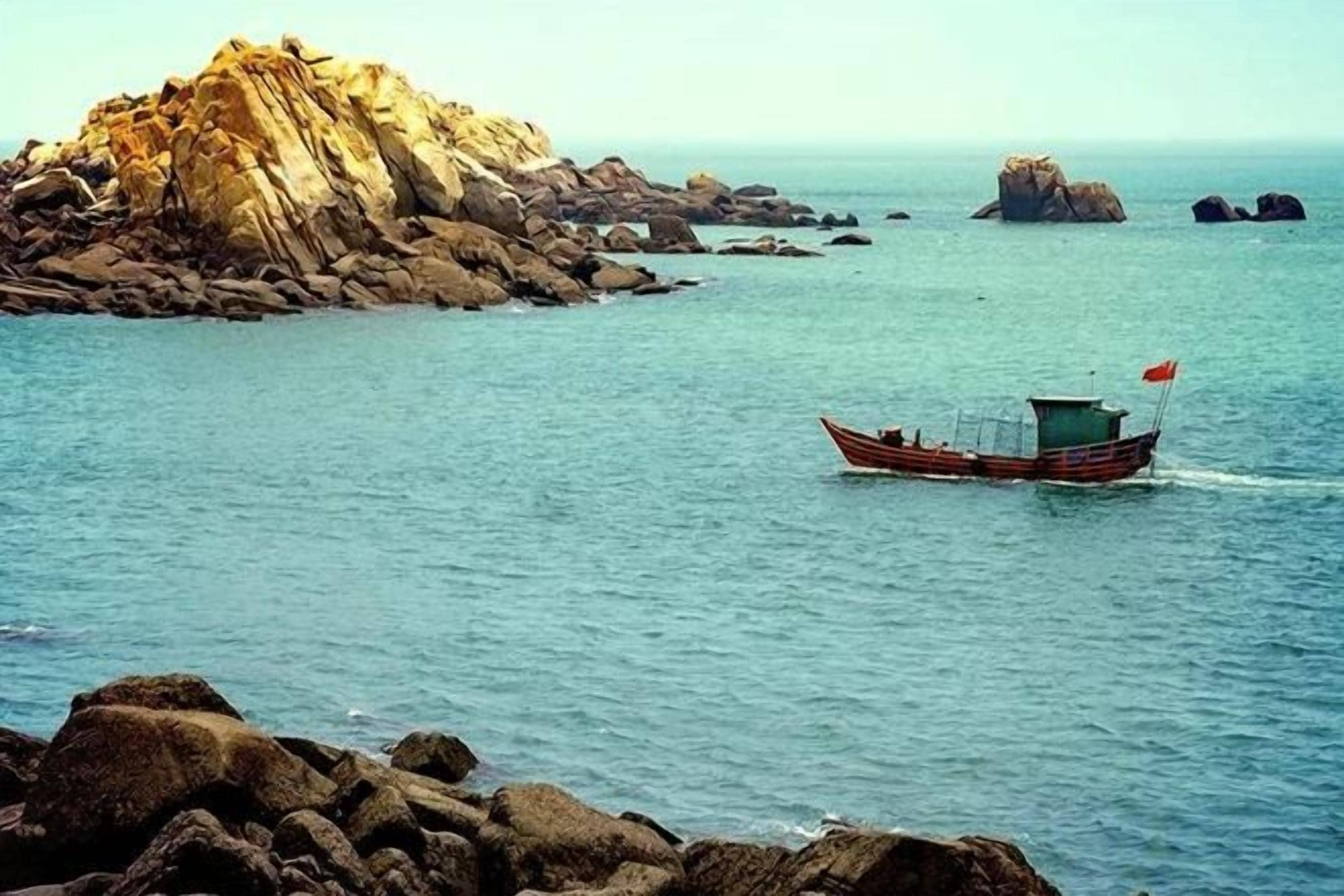 A boat on calm water near rocky terrain.