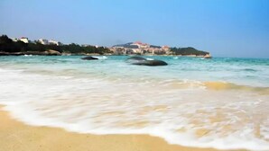 Une plage avec une eau turquoise et limpide, un rivage sablonneux et des bâtiments en arrière-plan.