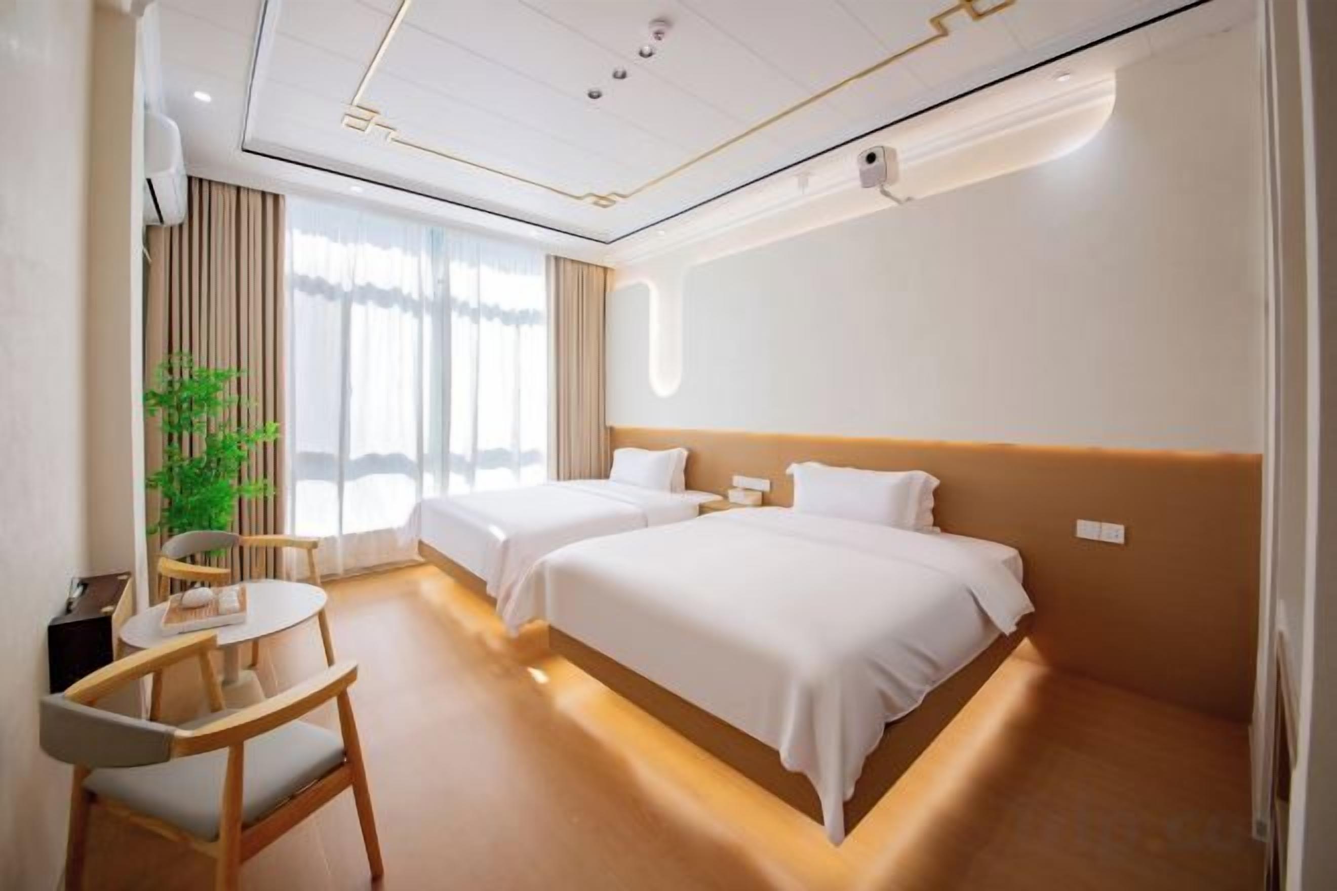 Une chambre d’hôtel avec deux lits, un bureau, une chaise et une grande fenêtre.