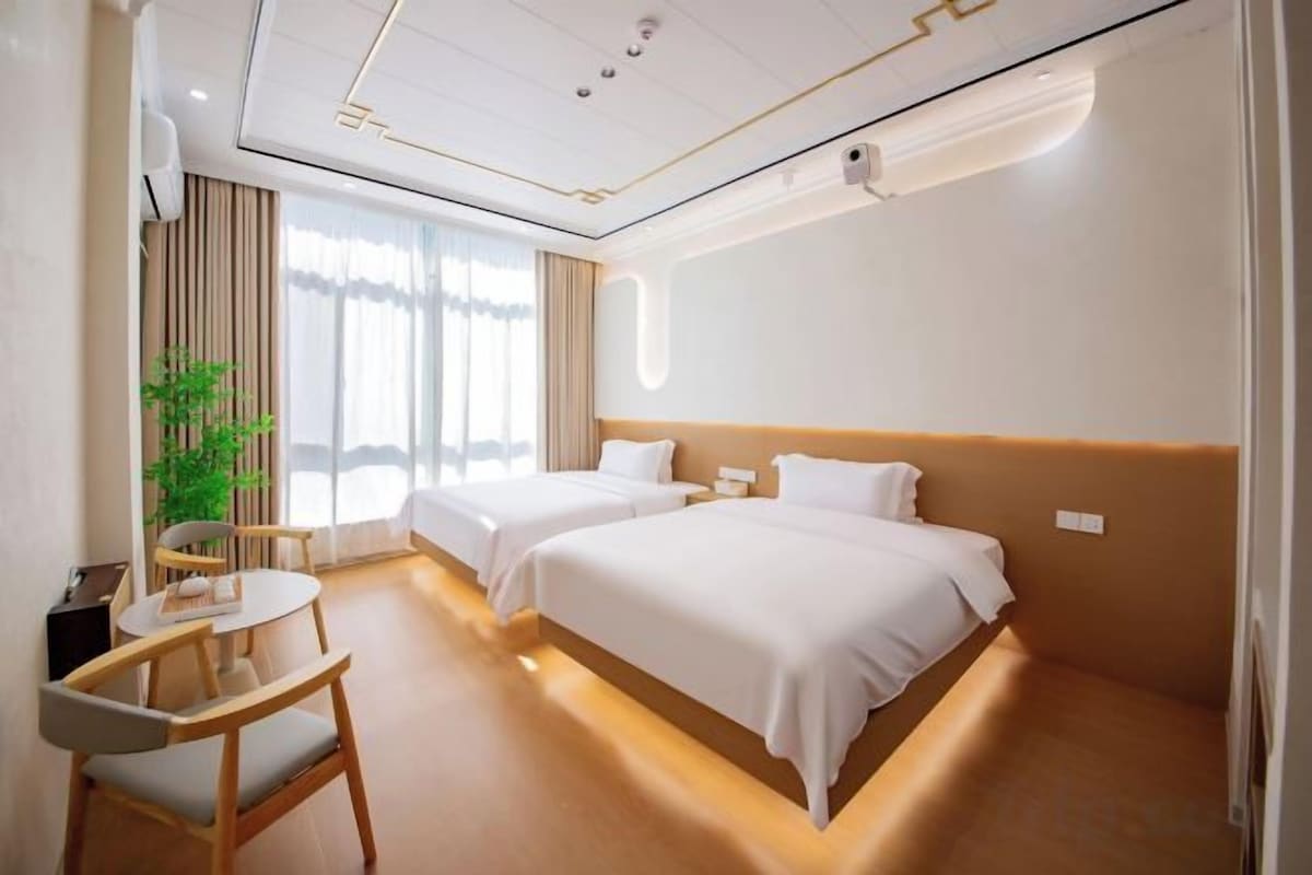 Ein Hotelzimmer mit zwei Betten, einem Schreibtisch, einem Stuhl und einem großen Fenster.