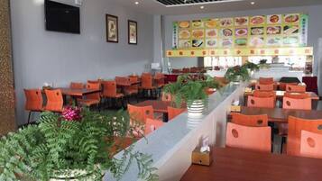 Un restaurante con varias mesas y sillas, una barra con plantas y una pantalla con el menú en la pared.