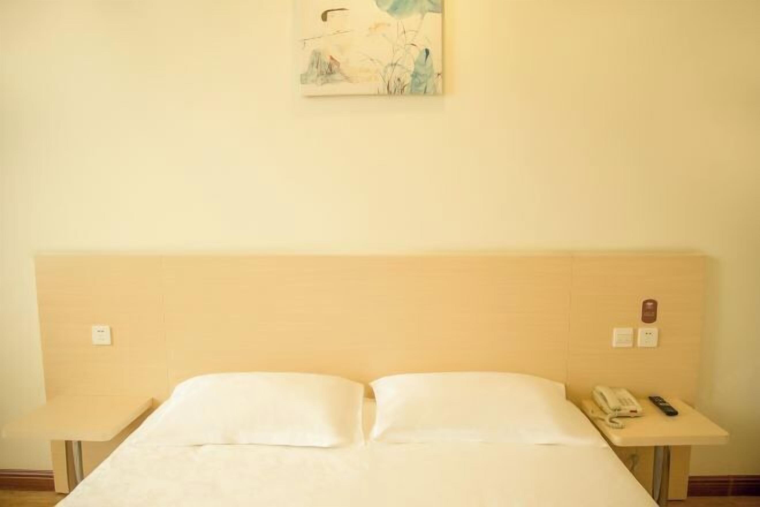 Una habitación de hotel con una cama, mesitas de noche, un teléfono y un cuadro en la pared.