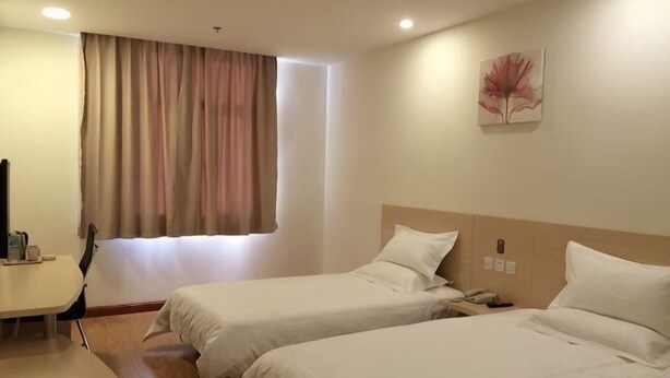 Une chambre d’hôtel avec deux lits, un bureau, une chaise, une fenêtre avec des rideaux et un téléphone fixé au mur.