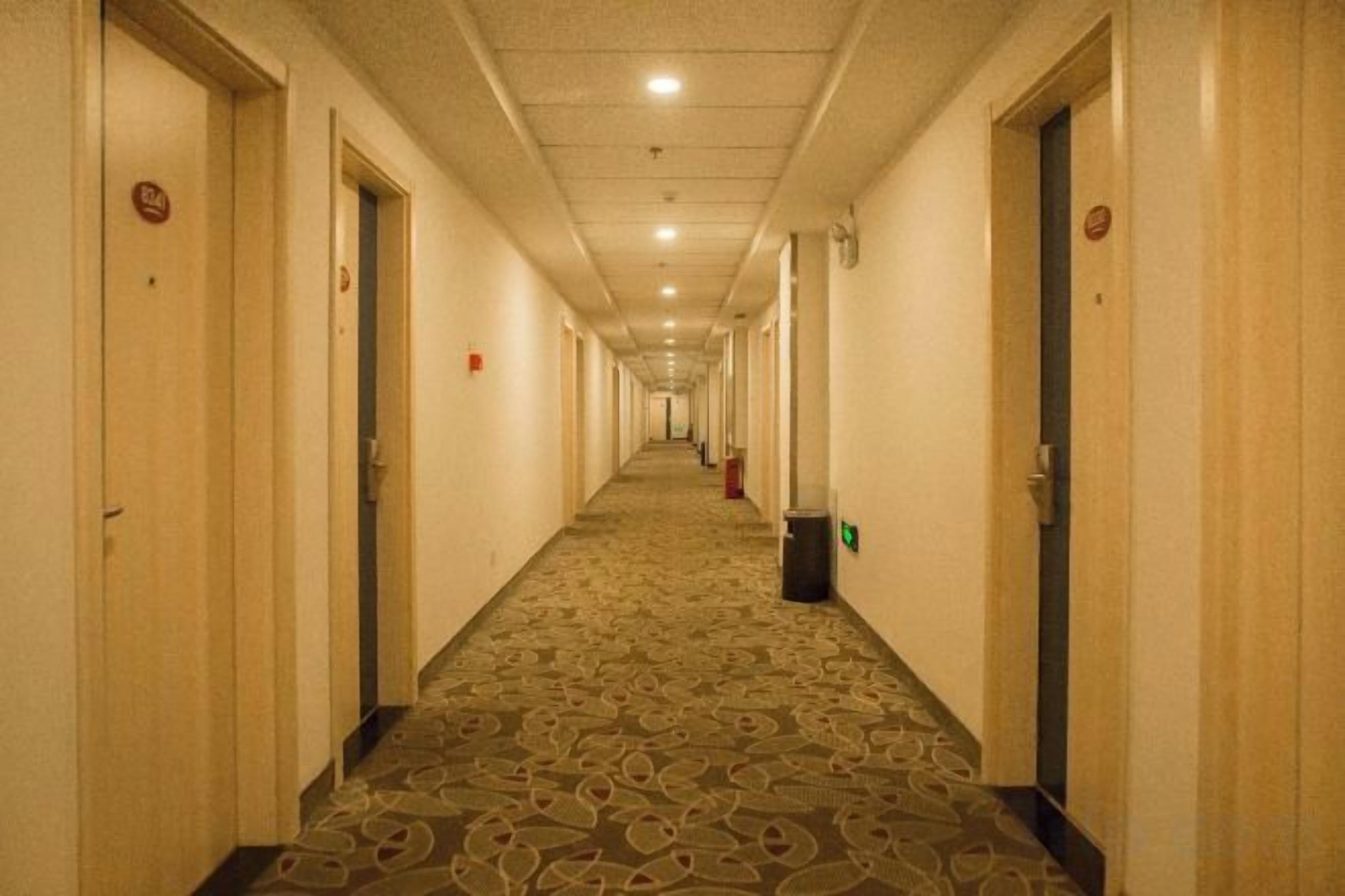Un pasillo de hotel con pisos alfombrados, puertas a ambos lados y un basurero en el centro.