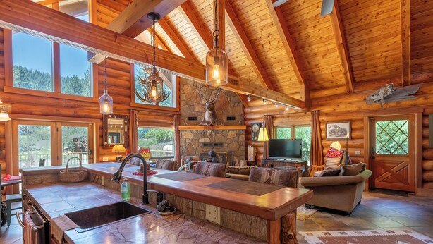 Interior espaiós d'una cabana de fusta amb una cuina gran, una llar de pedra i un saló acollidor amb una llar i televisió.