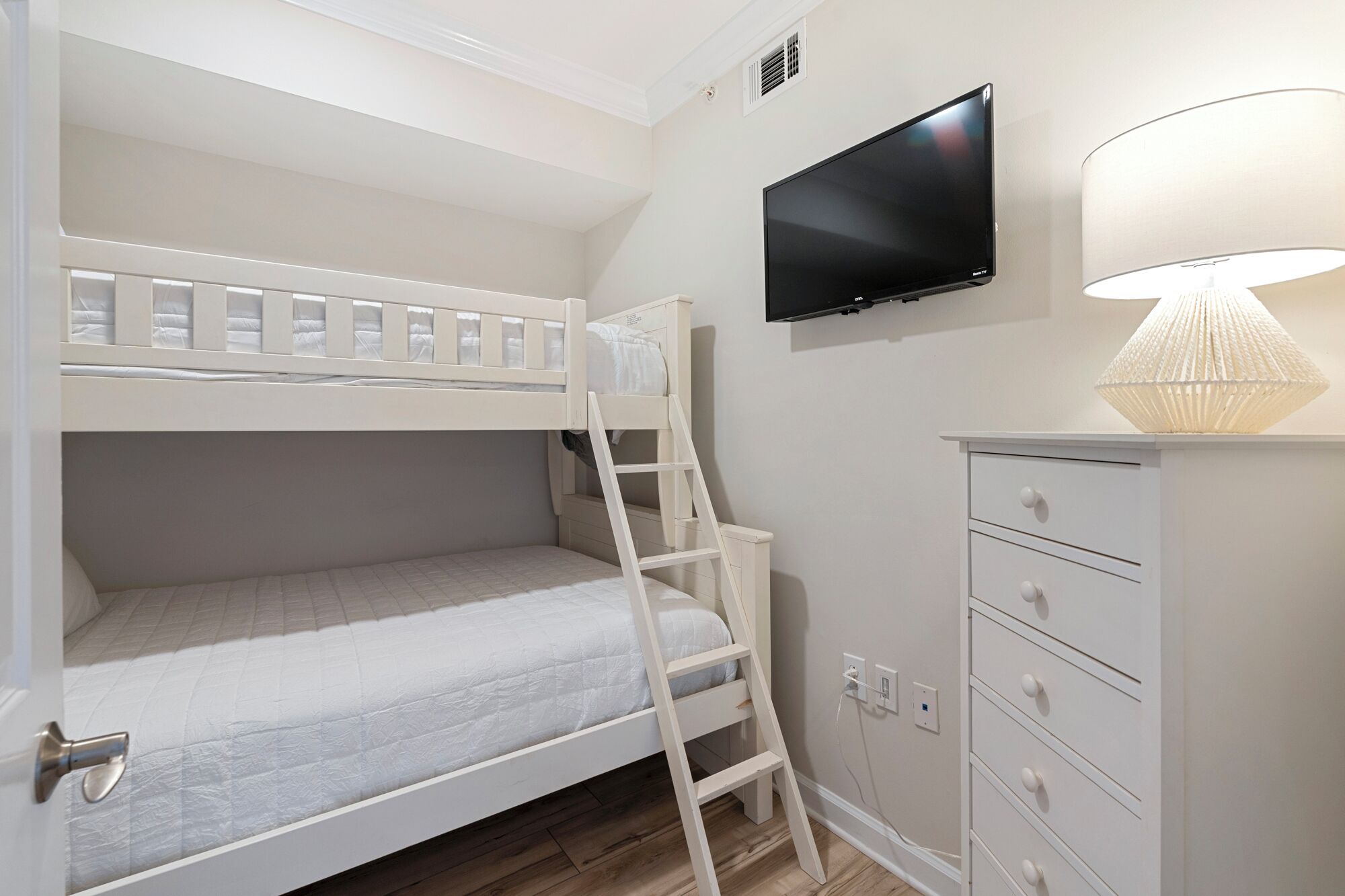 A bunk bed with a TV above it, a lamp, and a cabinet with drawers.