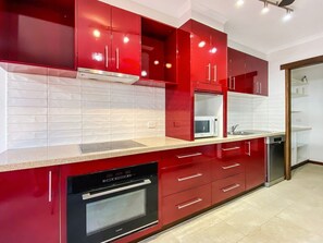 Een moderne keuken met rode kastjes, een magnetron, een vaatwasser en een inbouwoven.
