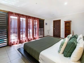 Een slaapkamer met een groot bed, een staande lamp en uitzicht door het raam.