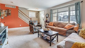 A living room with a sofa, armchair, and coffee table. There is a staircase leading to another level. - Charming Kalamazoo Home w/ Yard: 1 Mi to Downtown! (Kalamazoo)