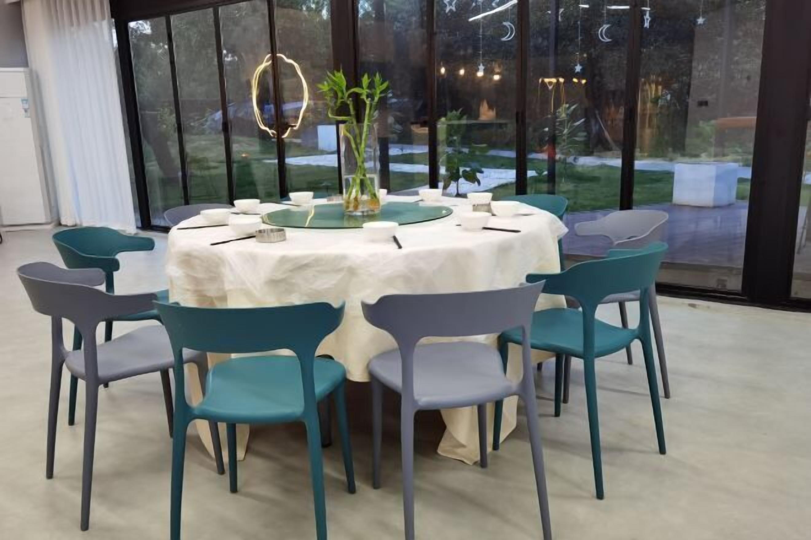 A round table with a white tablecloth surrounded by teal chairs in a room with large windows.