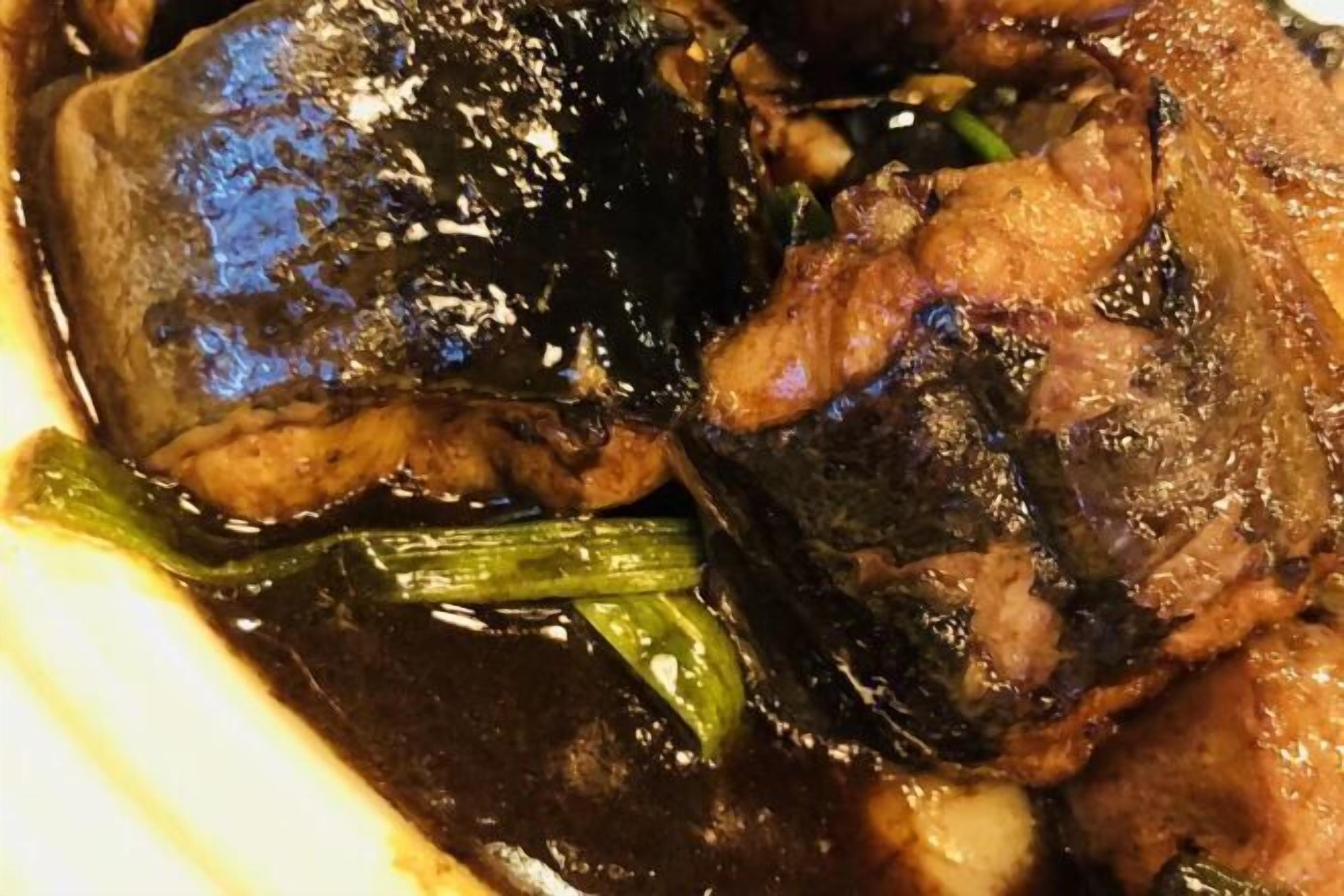 A close-up of a dish with meat and vegetables in a dark sauce.