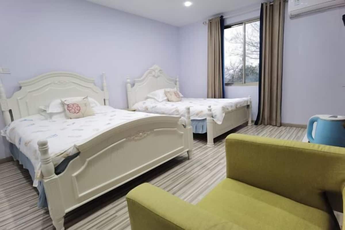 Hotellihuone, jossa on kaksi sänkyä, vihreä nojatuoli, ikkuna verhoilla ja patteri.