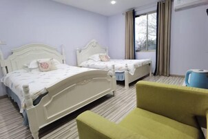 Habitación de hotel con dos camas, un sillón verde, una ventana con cortinas y un radiador.