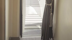 Een kamer met uitzicht door een raam, voorzien van dunne gordijnen, een donkere gordijn teruggebonden, en een houten vloer.