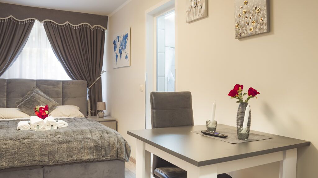 Habitación de hotel con cama, escritorio, silla, un jarrón con flores y obras de arte en las paredes.