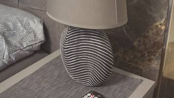 A modern lamp with a unique design on a bedside table, a remote control, and a patterned pillow on a couch.