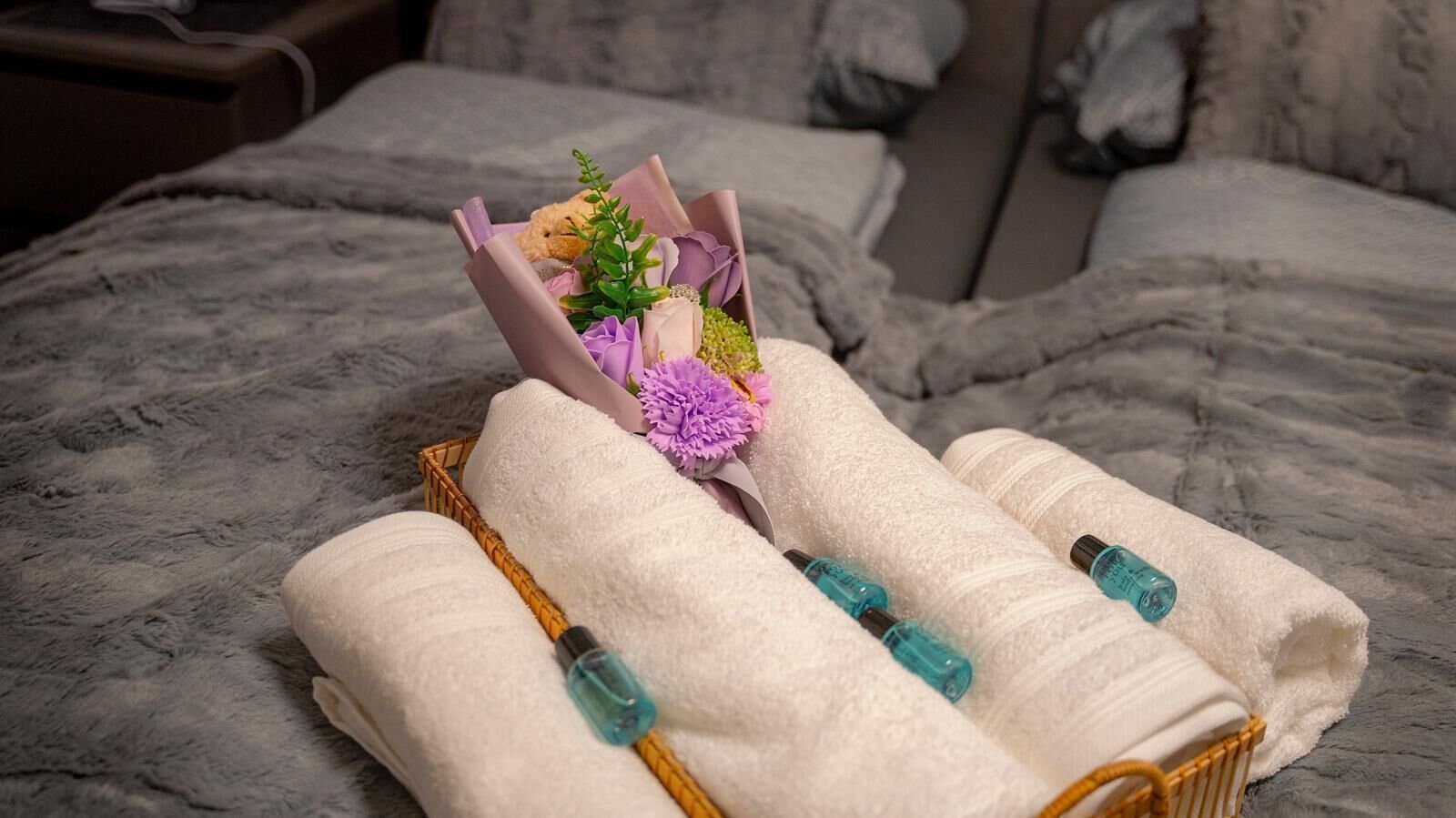 A neatly made bed with a bouquet of flowers, a basket, and two bottles of lotion.