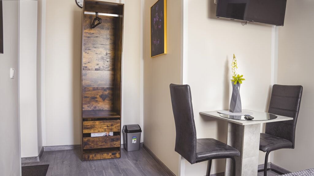 A modern room with a wooden accent wall, a round table with two chairs, a small trash bin, and a mounted TV.