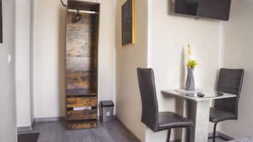 A modern room with a wooden accent wall, a round table with two chairs, a small trash bin, and a mounted TV.