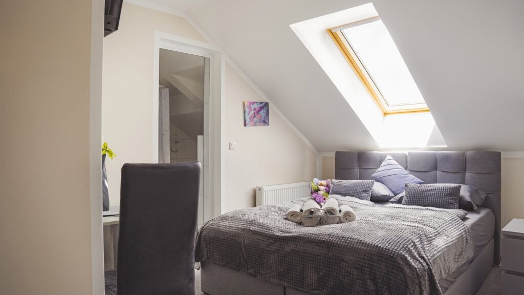 Un dormitorio con tragaluz, una cama con almohadas, una silla y un radiador.