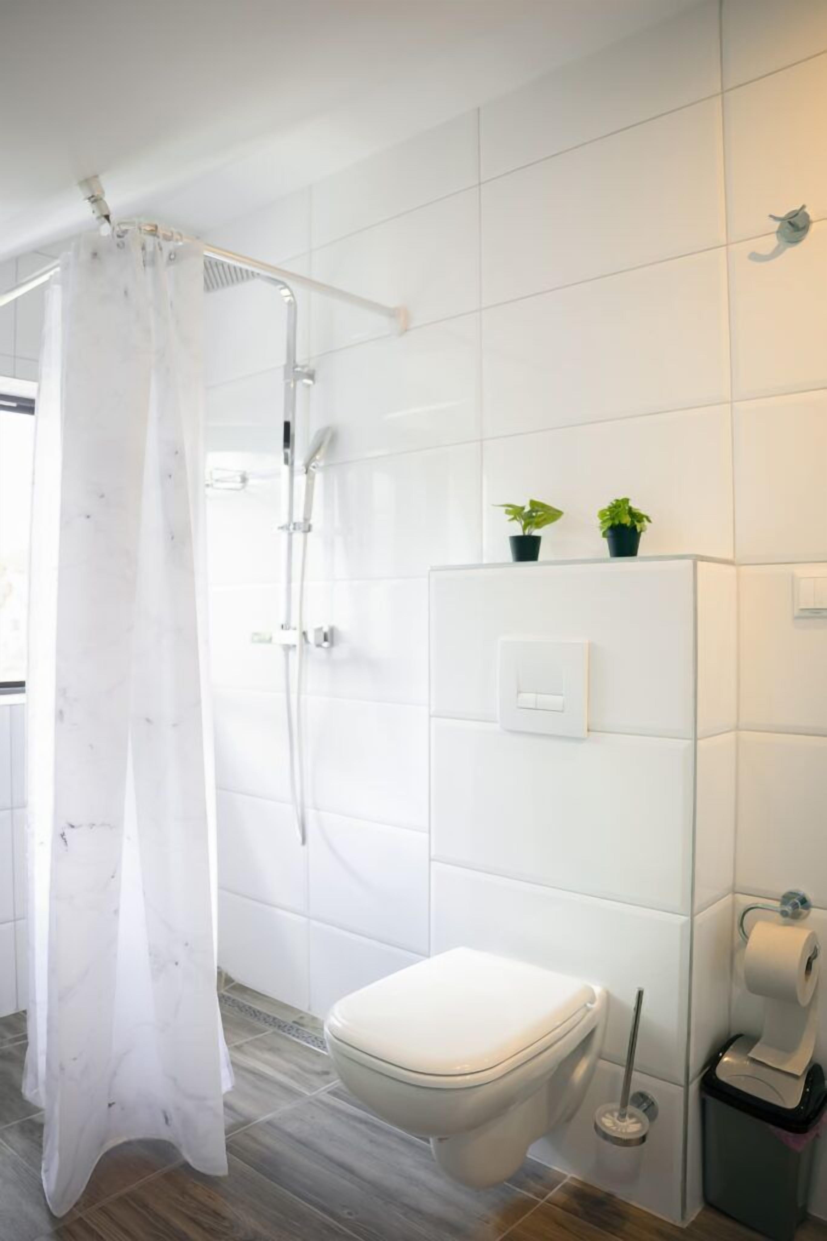 A modern bathroom with a shower, toilet, and a small trash bin.
