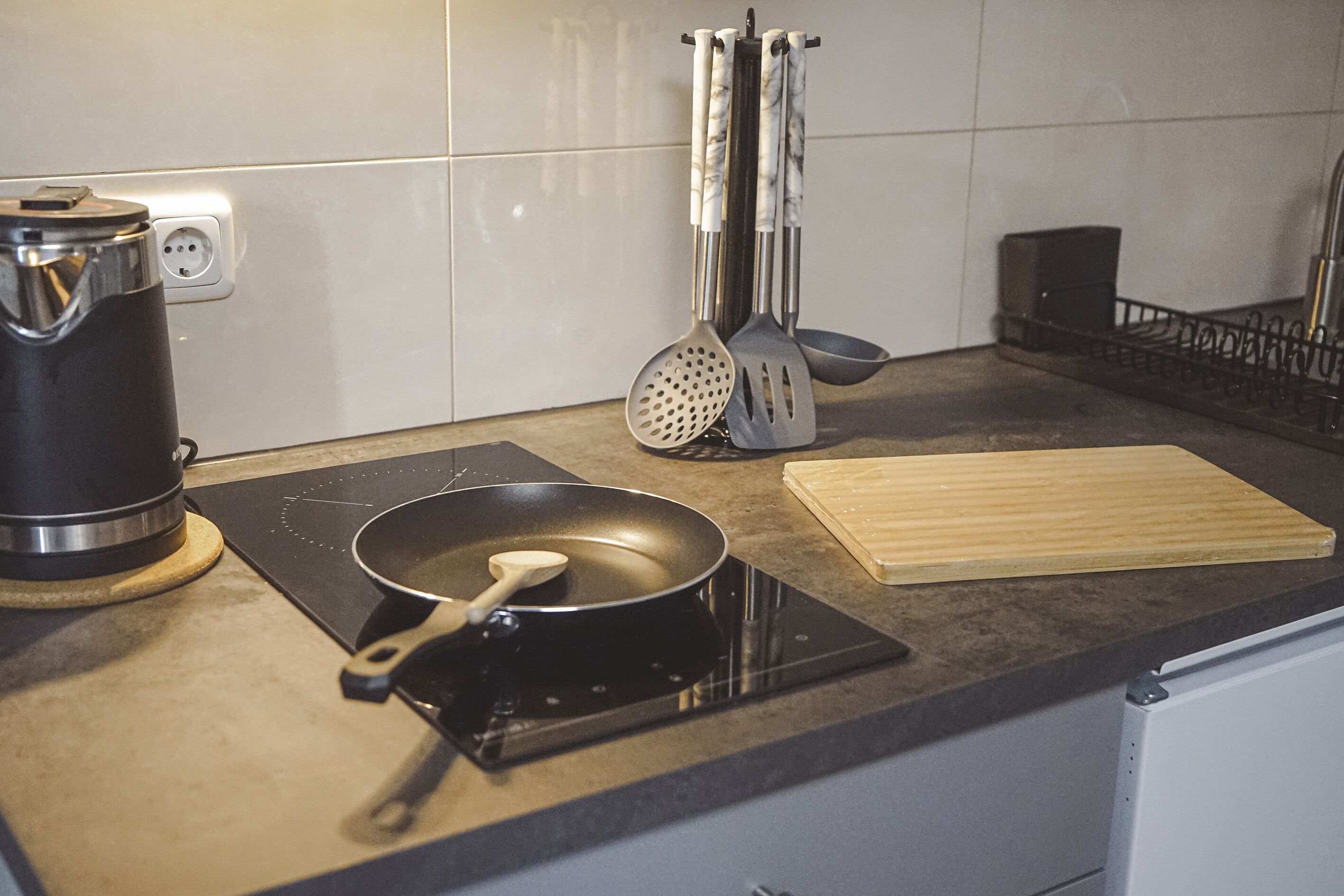 Una cucina con un fornello, una padella, un tagliere di legno e diversi utensili da cucina.
