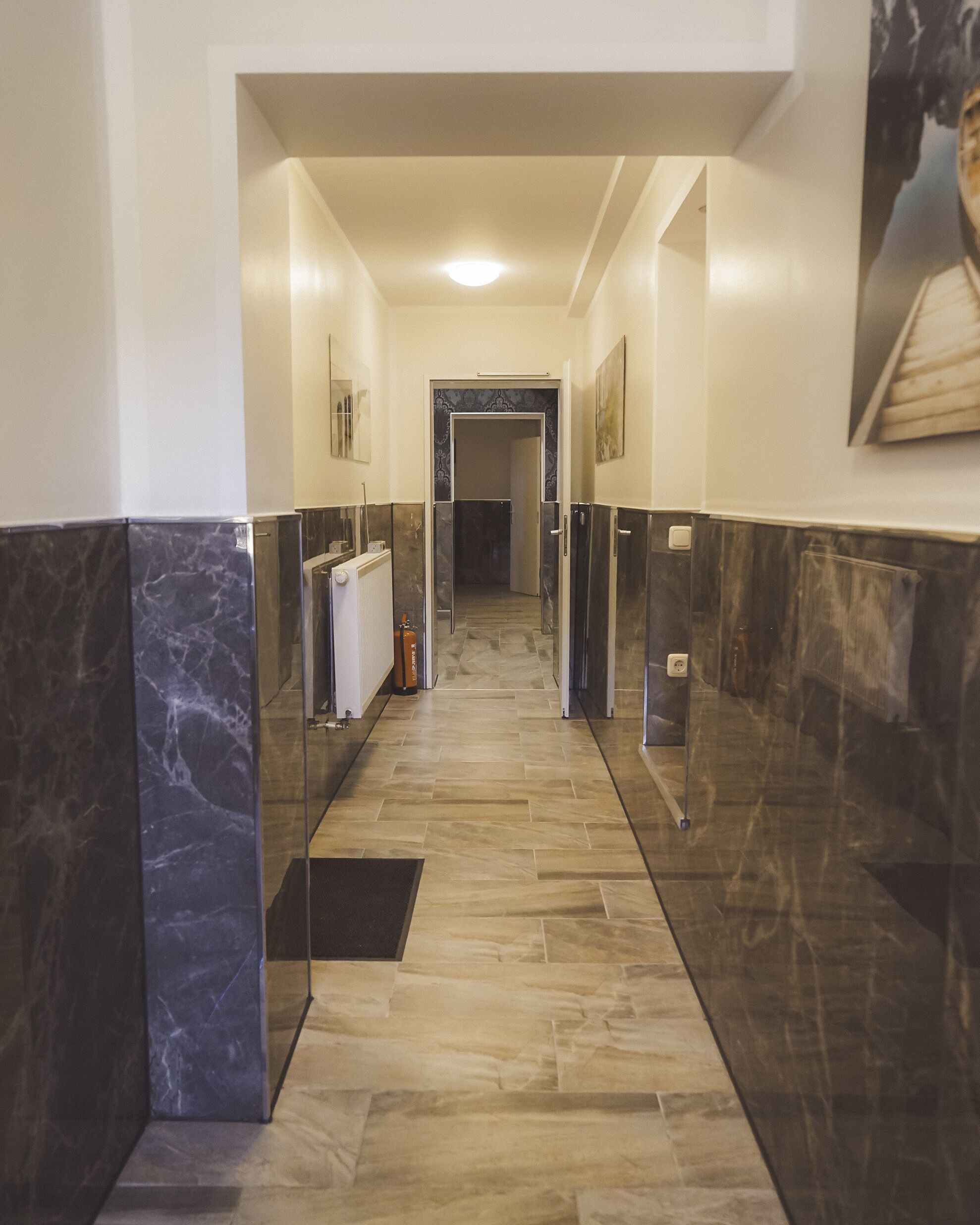 A hallway with marble walls and a tiled floor, leading to a door at the end.