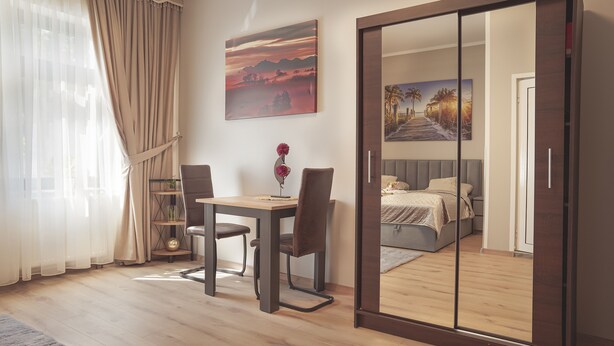 Een slaapkamer met een bed, een bureau en stoelen. Er hangt een schilderij aan de muur en een raam met gordijnen.