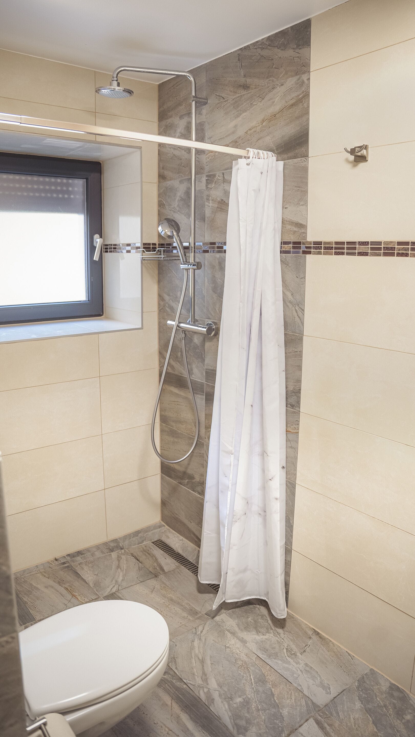 Un baño con ducha, inodoro y ventana.