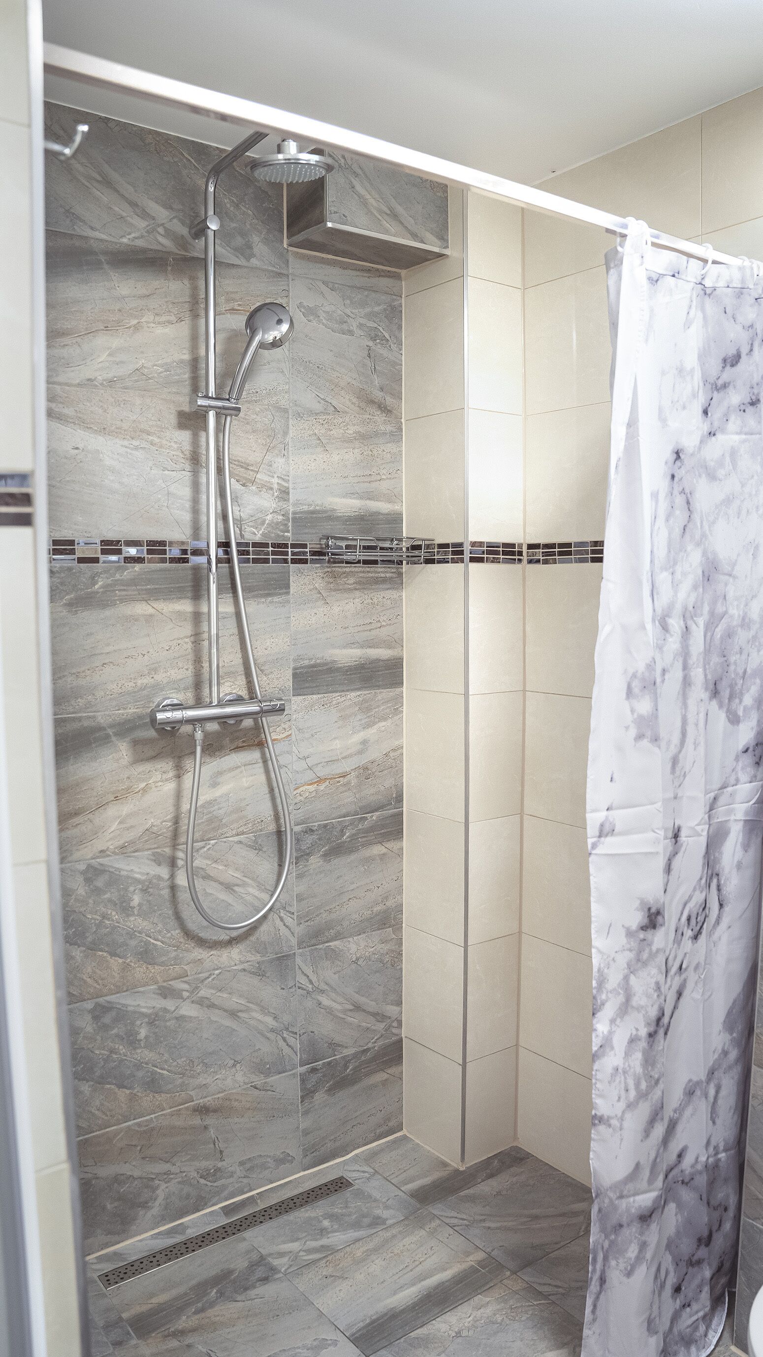 Ducha con cabezal de ducha manual y cabezal de ducha fijo, paredes de azulejos y cortina de ducha con diseño de mármol.