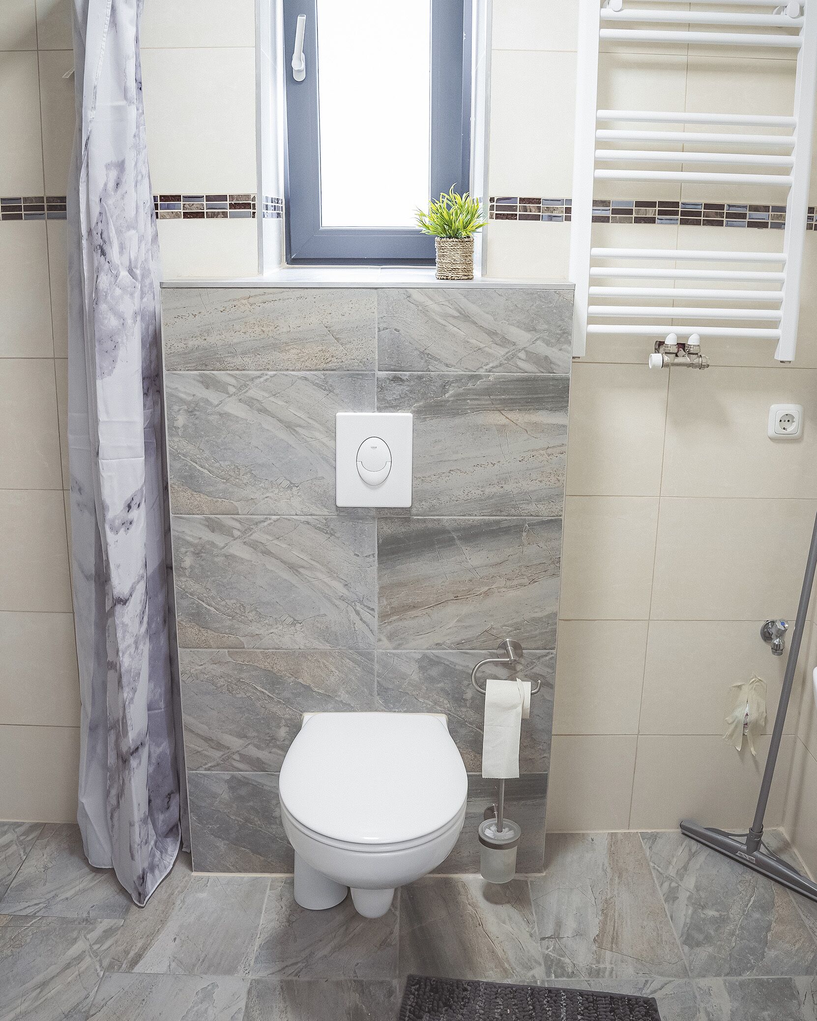 A bathroom with a toilet, a towel dispenser, a shower, and a window with a plant on the windowsill.