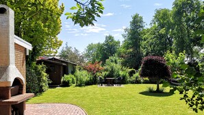 A brick patio with a stone oven, a wooden shed, and a well-maintained lawn with a round table and chairs. - Apartment in Esens, Deutschland (Esens)