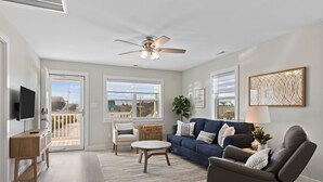 A spacious living room with a large window, a ceiling fan, a TV, a sofa, a coffee table, and a chair. - Walk on the Beach "Downtown" - your feet in the sand in 250 ft.  Pet friendly (Atlantic Beach)