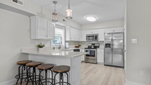 A modern kitchen with white cabinetry, stainless steel appliances, a central island with stools, and pendant lighting. - Walk on the Beach "Downtown" - your feet in the sand in 250 ft.  Pet friendly (Atlantic Beach)