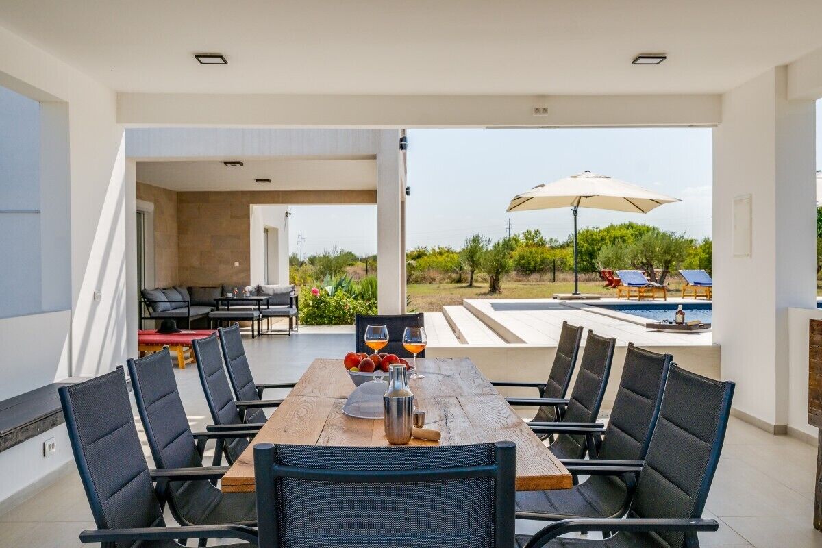 Ein Essbereich mit Holztisch, schwarzen Stühlen und Blick auf Pool und Garten.