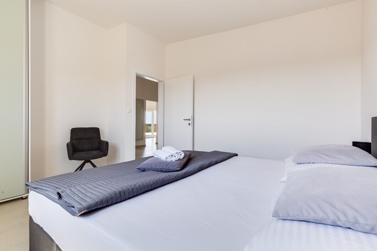 A modern hotel room with a large bed, a chair, and a door leading to another room.