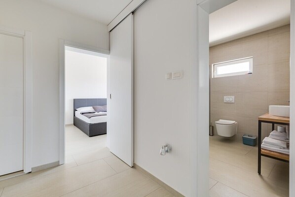 A modern bedroom with a bed, a bathroom with a toilet and sink, and a hallway leading to another room.