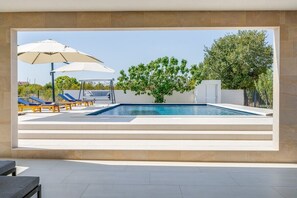 A swimming pool with lounge chairs and umbrellas, surrounded by a stone wall and trees.