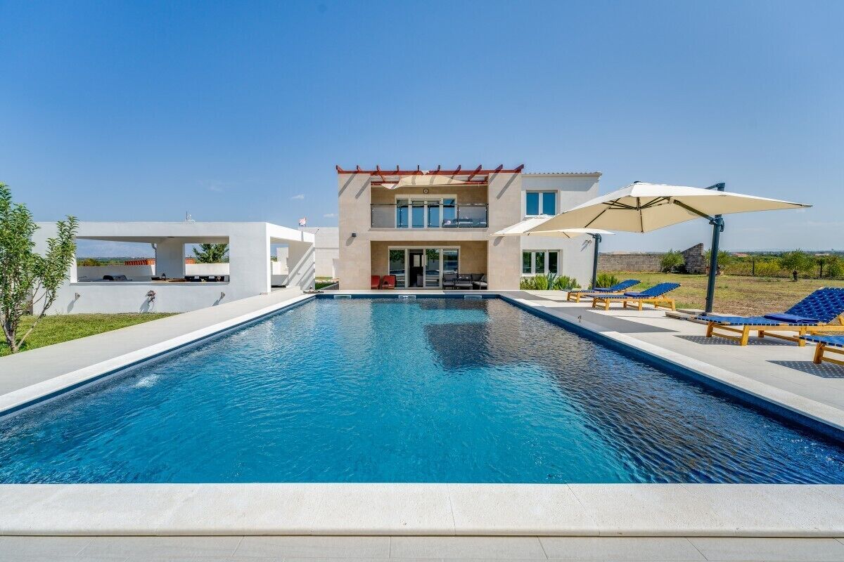 A modern two-story house with a swimming pool, outdoor seating, and a clear view of the surrounding landscape.