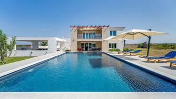 A modern two-story house with a swimming pool, outdoor seating, and a clear view of the surrounding landscape.