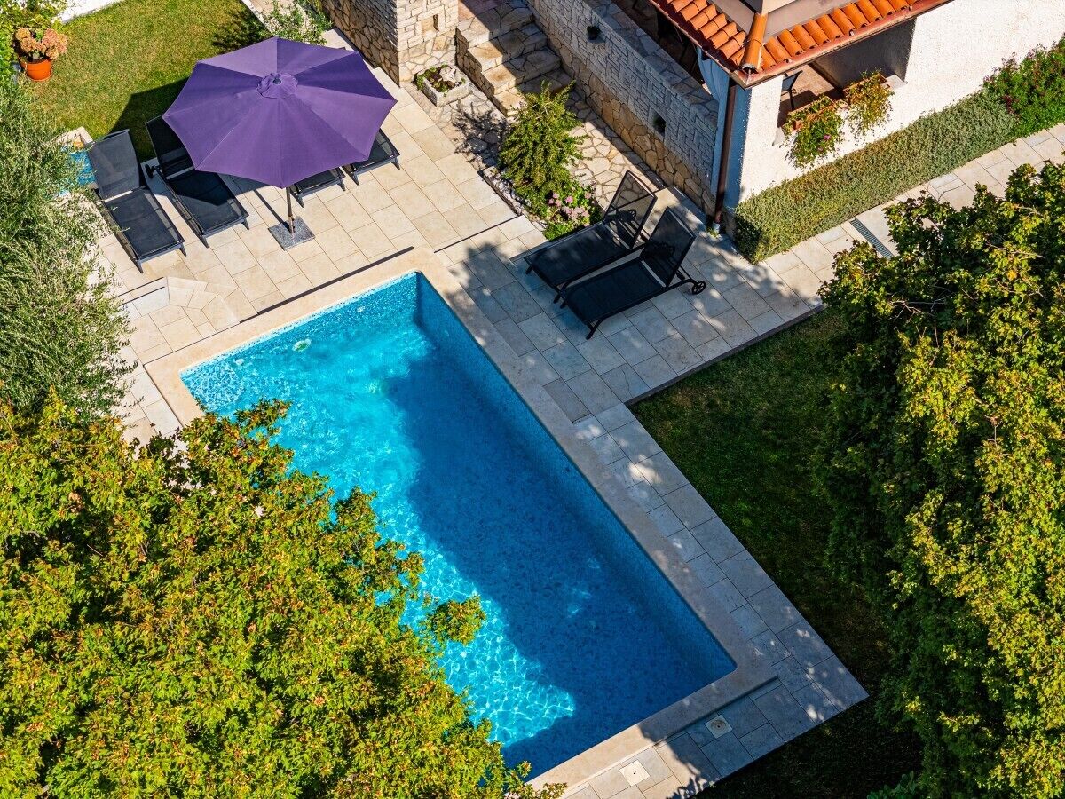 Vue aérienne d’une piscine avec des chaises longues et un parasol violet.