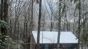 Una cabaña rodeada de un bosque denso con suelo cubierto de nieve.