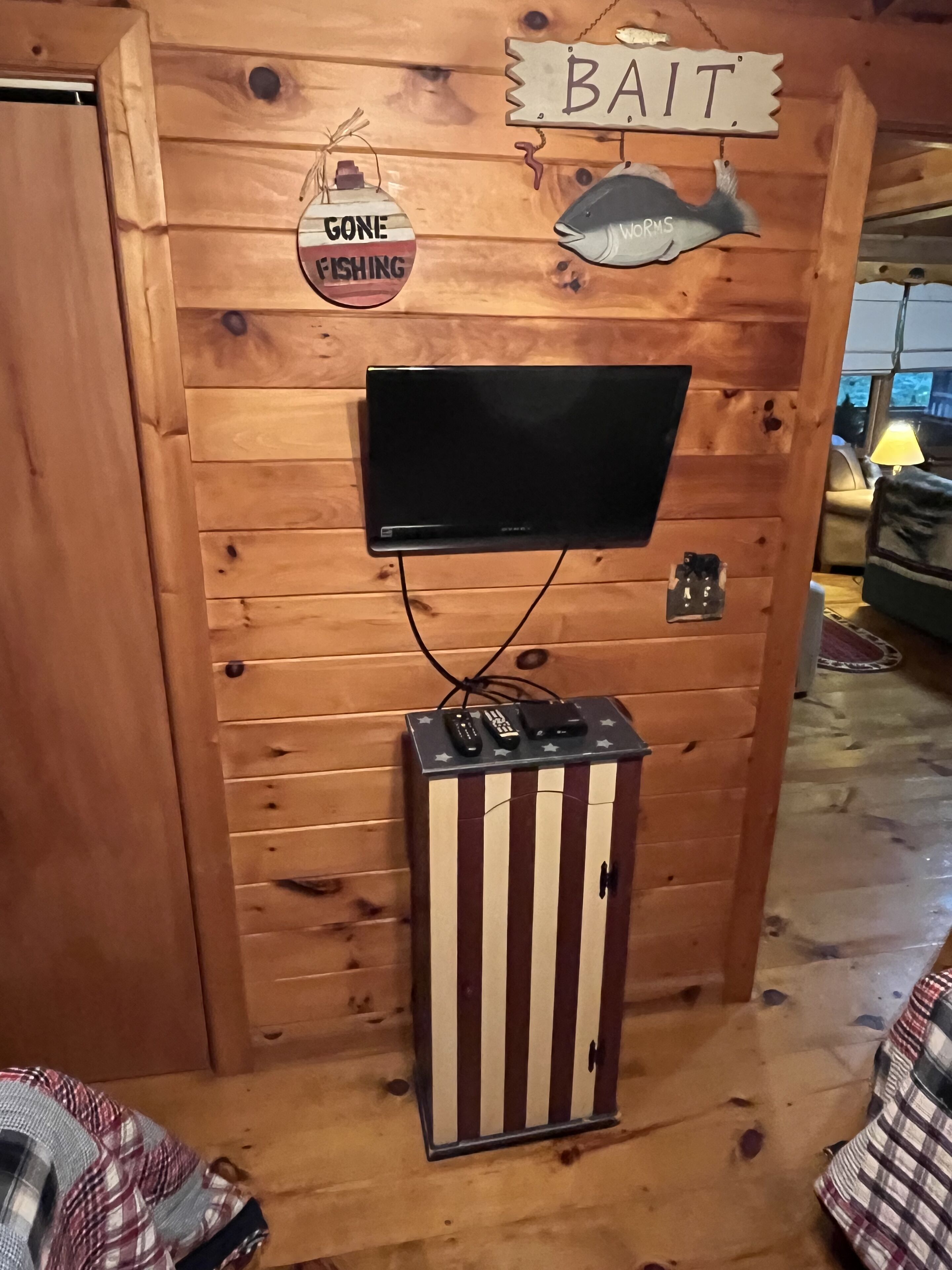 A wooden wall with a mounted television, a small cabinet with star decorations, and signs reading "BAIT" and "GONE FISHING".