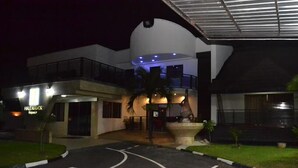 A modern hotel with a curved facade, a covered entrance, and a well-lit outdoor area with a palm tree. - Hale Manor Exquisite (Benin City)