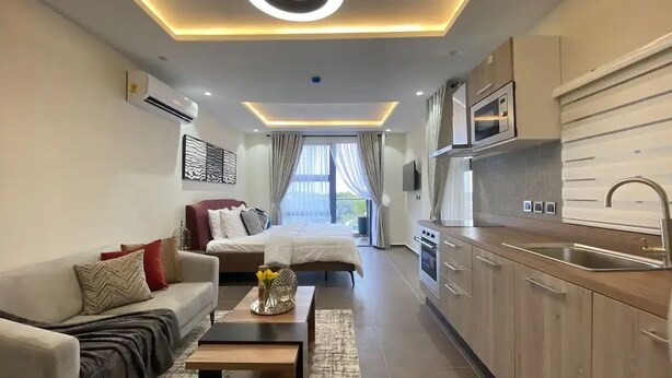 Een moderne hotelkamer met een bank, een bed, een salontafel en een keukenhoek met een spoelbak en magnetron.