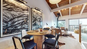 Un espace de salle à manger moderne avec une table ronde en bois, des chaises noires à coussins et de grandes œuvres d’art abstraites accrochées au mur.