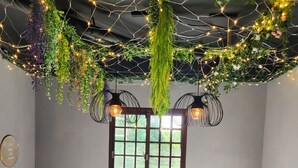 Un espace repas avec une longue table, six chaises, des plantes suspendues et des luminaires suspendus.