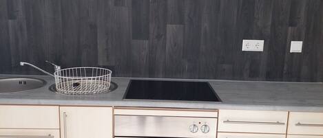 Una cocina con diseño moderno, que incluye un lavamanos de acero inoxidable, una hornilla negra y un horno empotrado.
